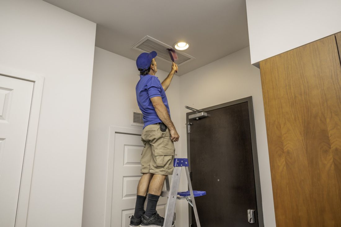 Tradie on a ladder cleaning an air conditioning duct